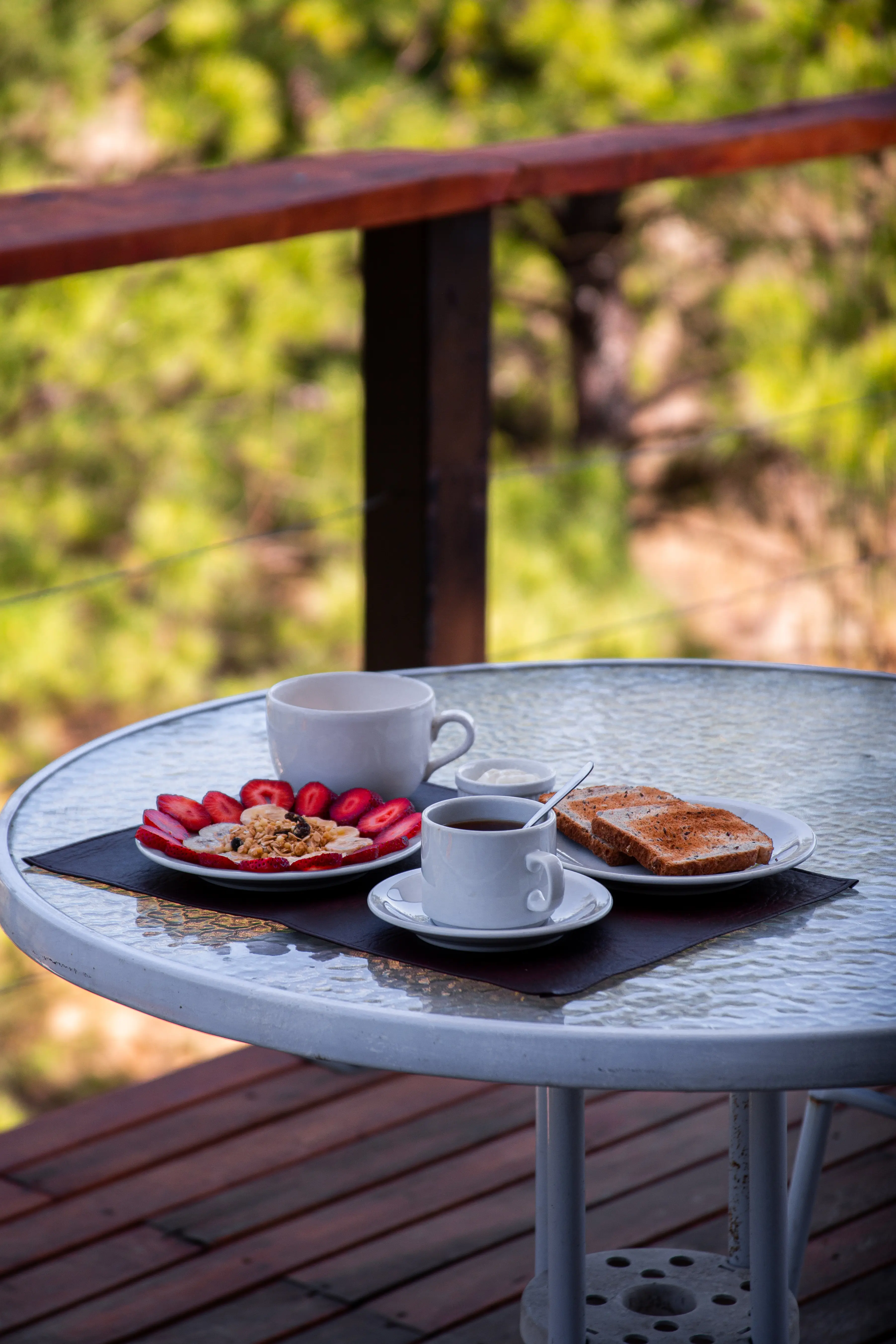 Desayuno servido en la mesa del deck, con los pinos de fondo